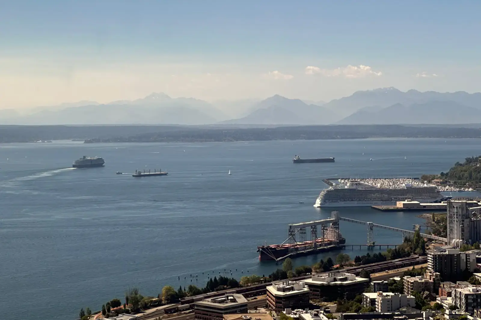 Elliot Bay in Seattle. Large ships in blue water with mountains in the background.