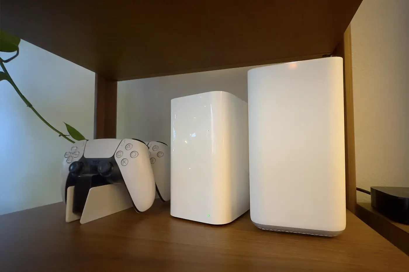 Apple Time Machine sitting next to some Playstation 5 controllers on a wooden bookshelf.