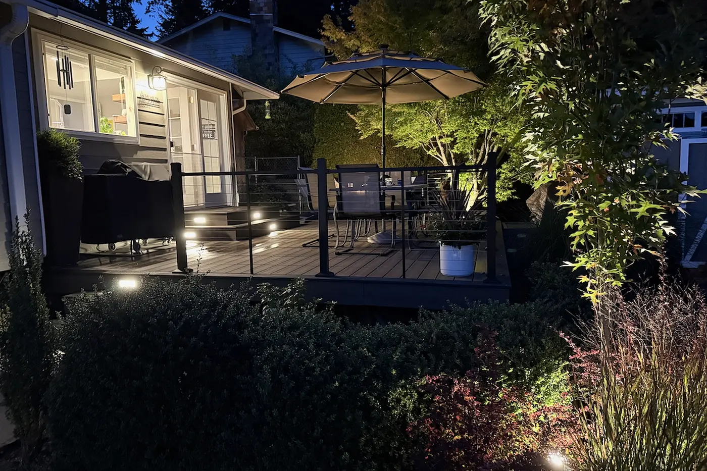 A picture of a new deck at night. Landscape lighting illuminates plants around.