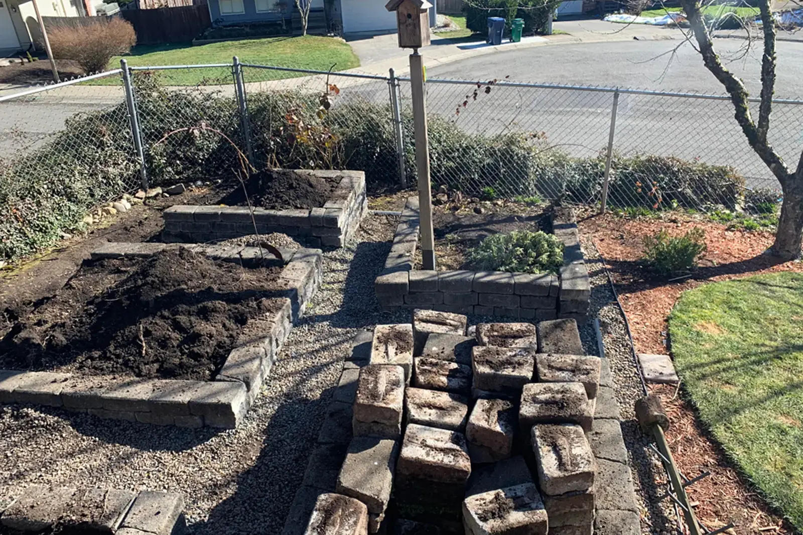 A corner of the yard with some retaining wall blocks and piles of dirt.